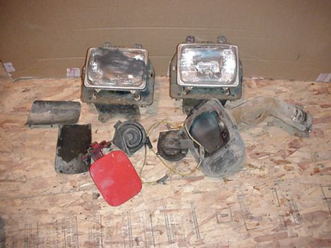 1979 Ford Bronco - Various car parts, including headlights and horns, are displayed on a plywood surface.