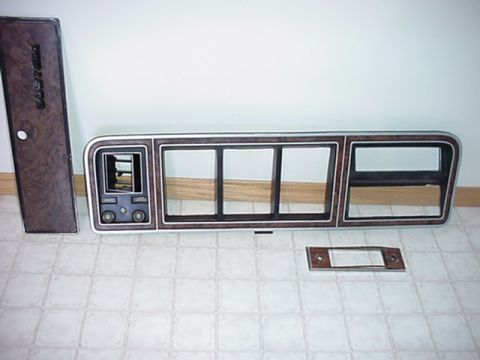 1979 Ford Bronco - Woodgrain dashboard trim pieces are laid out on a tiled floor, showing various openings for gauges and controls.