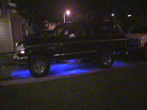 1994 Ford Bronco - This black SUV, likely from the early to mid-1990s, is parked at night with blue underglow lighting illuminating the ground beneath it.