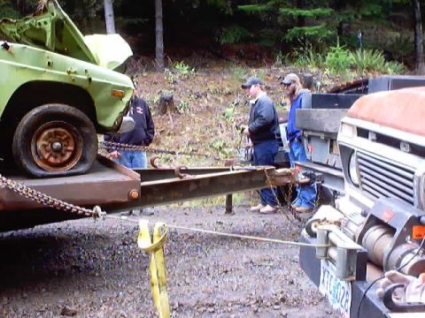 1976 Ford F-100 - Two trucks are being loaded onto a trailer in a wooded area.