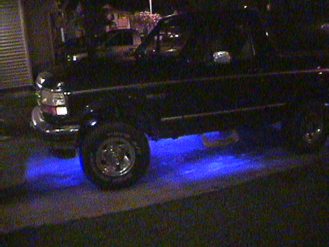Black SUV with blue underglow, side view, showing chrome wheels and body trim