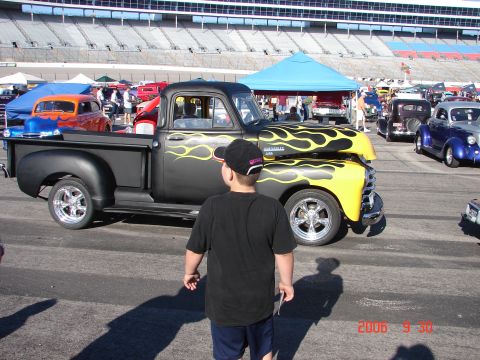 1987 Ford Bronco - A custom pickup truck with flame graphics is displayed at an outdoor event with spectators and other vehicles.
