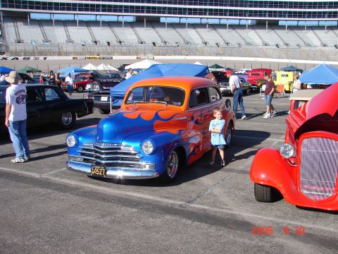 1987 Ford Bronco - A custom hot rod with flame graphics is parked at an outdoor event with a stadium in the background.