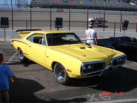 1987 Ford Bronco - Yellow 1970 Dodge Super Bee muscle car parked at a racetrack with other vehicles visible.