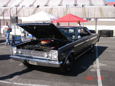 1987 Ford Bronco - A black 1966 Plymouth is displayed with its hood up at an outdoor event, with stadium seating in the background.