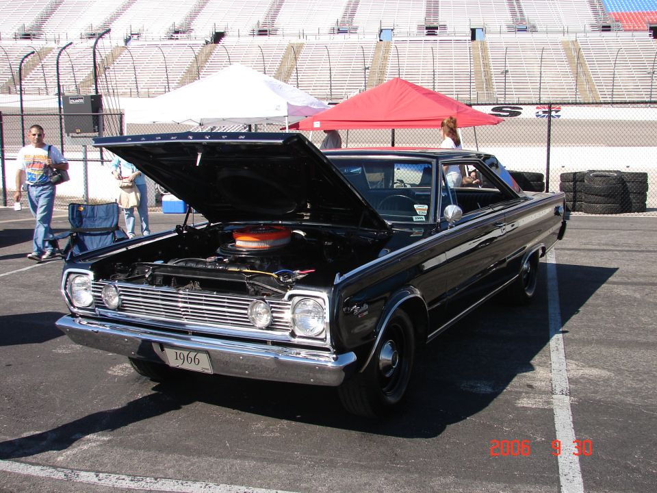 black 1966 Plymouth with hood open, parked at a racetrack