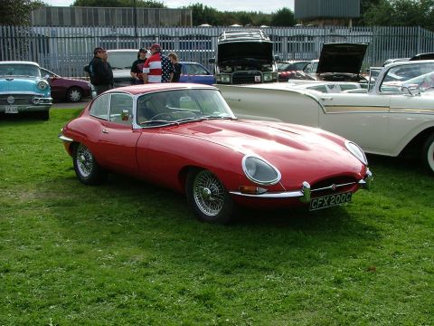2001 Ford Fiesta - Red classic Jaguar E-Type Series 1 coupe parked on grass with other vehicles present.