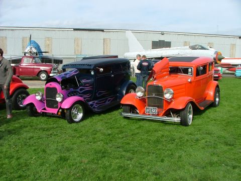 2001 Ford Fiesta - Two vintage hot rod sedans are displayed on a grassy field with airplanes in the background.