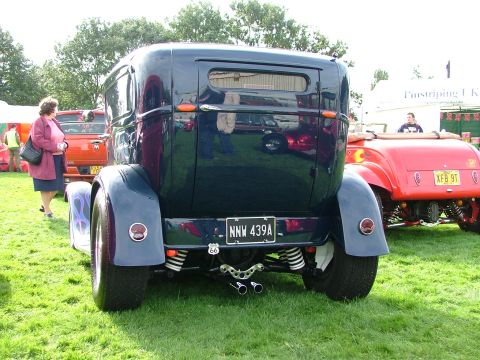 2001 Ford Fiesta - A dark blue hot rod sedan is seen from the rear, parked on grass next to a red convertible.