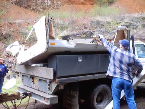 1976 Ford F-100 - Two people are loading a camper shell onto the bed of a flatbed truck.