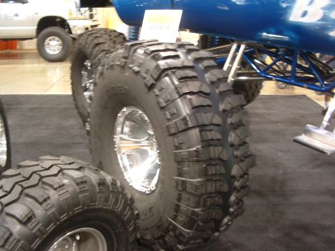 2004 Toyota Tacoma - Oversized off-road tires and chrome rims are prominently displayed on a custom vehicle, with another truck visible in the background.