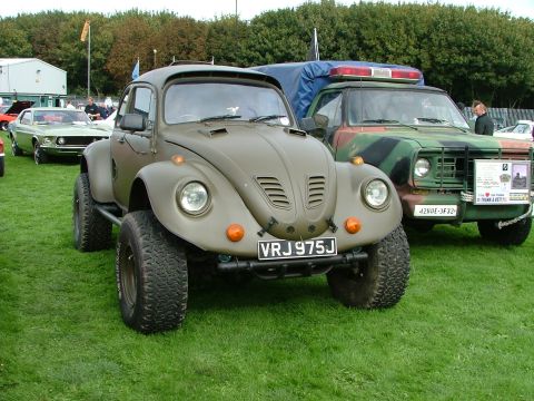 2001 Ford Fiesta - A modified Volkswagen Beetle sits on a grassy field next to a camouflage-painted truck.