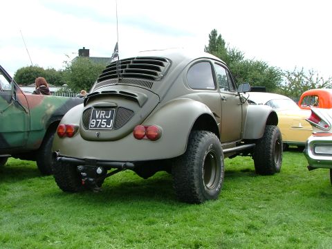 2001 Ford Fiesta - Modified Volkswagen Beetle with large tires and custom rear window sits on a grassy field next to other vehicles.