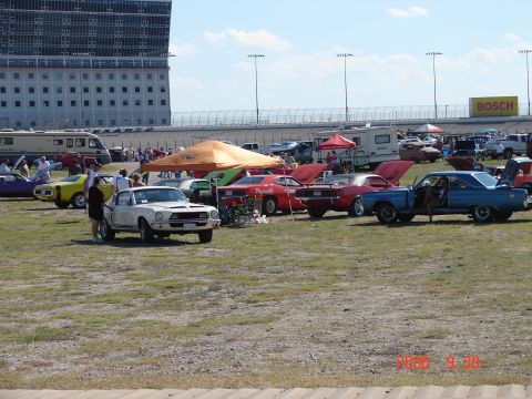 1987 Ford Bronco - A white 1967 muscle car is parked on a grassy field with other classic vehicles and spectators.
