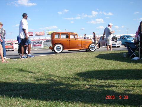 1987 Ford Bronco - Hot rod sedan with whitewall tires at an outdoor event with spectators and other vehicles.