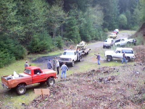 1976 Ford F-100 - A group of trucks and SUVs are gathered on a dirt road in a wooded area.