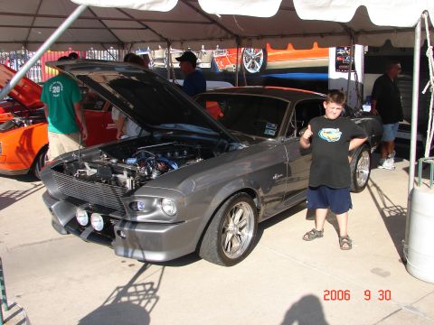 1987 Ford Bronco - A young boy gives a thumbs up next to a modified 1967 Ford Mustang Fastback at an outdoor car show.