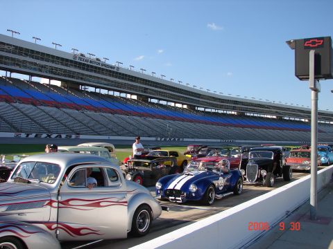 1987 Ford Bronco - Hot rods line up at Texas Motor Speedway under a clear blue sky.