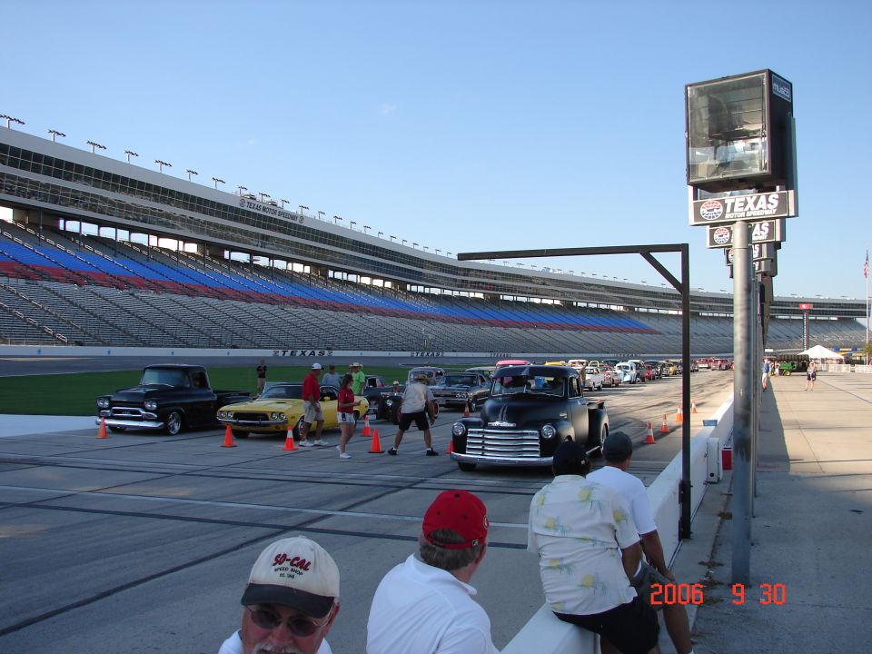 Cars lined up on a track in front of stadium seating, with a large Texas sign on a pole