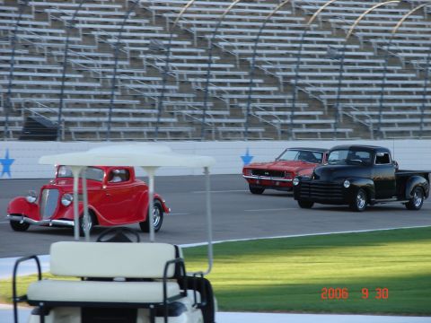 1987 Ford Bronco - Multiple classic vehicles on a racetrack, with grandstands and a golf cart visible.
