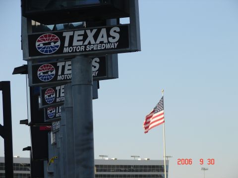 1987 Ford Bronco - Signs for Texas Motor Speedway and an American flag are visible against a clear sky.