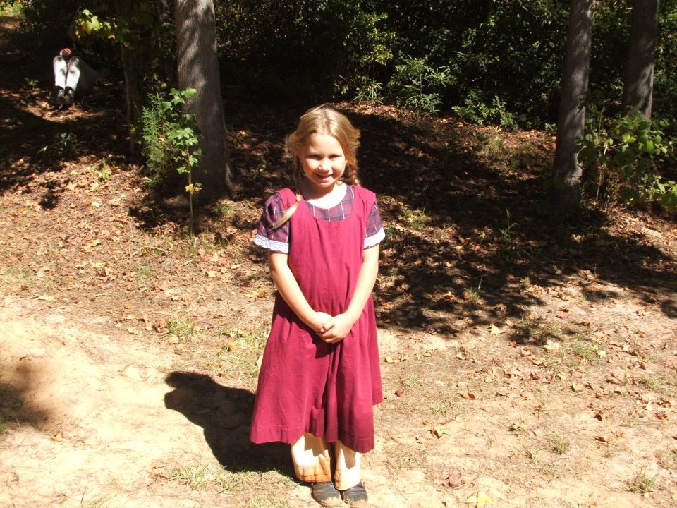 Girl in a red dress and white shirt stands in a wooded area
