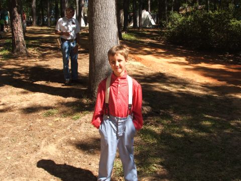 1966 Ford Ranchero - A young boy dressed in period clothing stands in a wooded area, with a man and tents visible in the background.