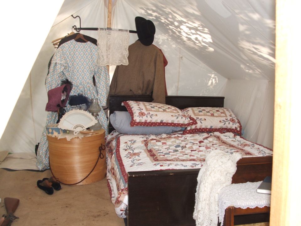 Interior of a tent with a bed, period clothing, and a fan