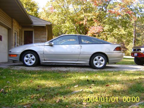 1990 Ford Probe - A silver 1990 Ford Probe is parked in front of a house, with another vehicle visible to the right.