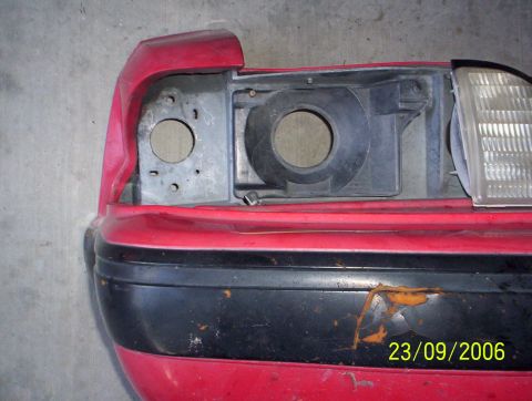 1990 Ford Mustang - Close-up of a red car bumper and headlight assembly, revealing damage and rust.