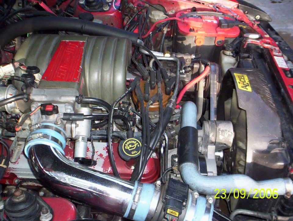 Engine bay with red intake manifold, chrome piping, and battery