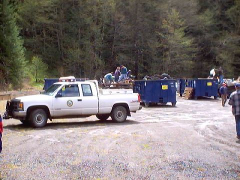 1976 Ford F-100 - People are loading a white pickup truck near several large blue dumpsters in an outdoor area.