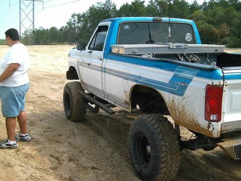 1986 Ford Bronco - This lifted pickup truck features a distinctive two-tone blue and white paint scheme and is equipped with a toolbox in the bed.