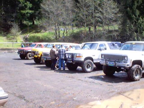 1976 Ford F-100 - A group of pickup trucks are parked in an outdoor lot, with several people gathered near them.
