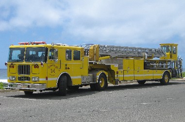 1991 Ford Bronco - A yellow fire truck with a long ladder is parked outdoors under a blue sky with some clouds.