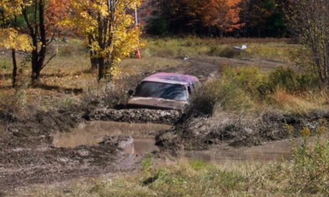 1979 Ford Bronco - A pink SUV is deeply mired in mud on an off-road trail during autumn.