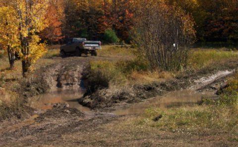1979 Ford Bronco - A pickup truck navigates a muddy trail with trees displaying fall colors in the background.