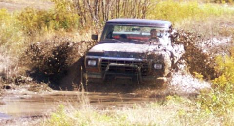 1979 Ford Bronco - Ford Bronco navigating a muddy trail, splashing water and dirt.