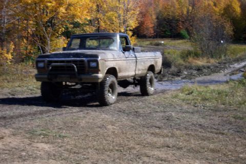 1979 Ford Bronco - A lifted, mud-covered Ford pickup truck navigates a wet, off-road trail during autumn.