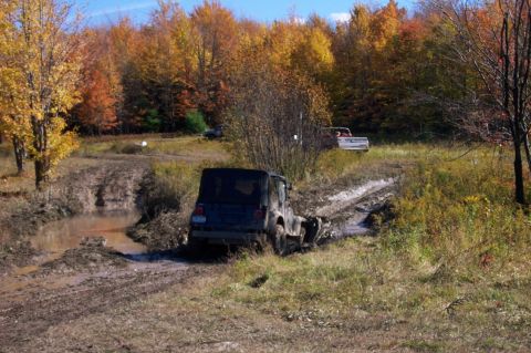 1979 Ford Bronco - A dark SUV navigates a muddy trail during the fall season, with another vehicle visible in the distance.