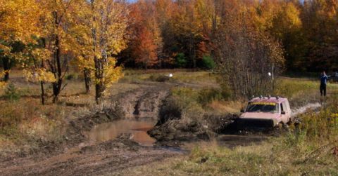 1979 Ford Bronco - A red SUV navigates a muddy obstacle course during autumn.