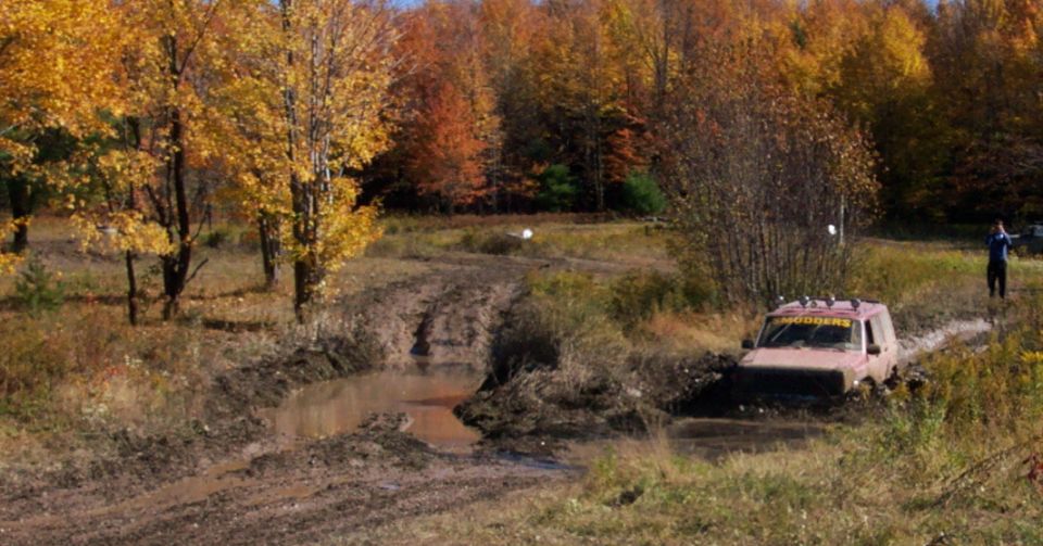 Red SUV stuck in mud pit with fall foliage in background