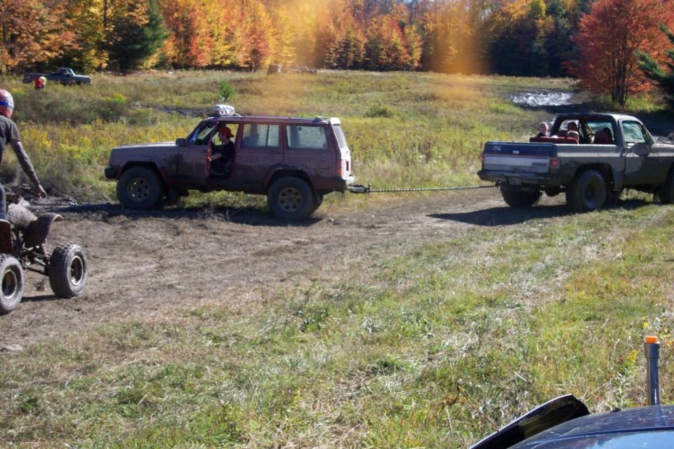 Red SUV being towed by a pickup truck in a muddy field with fall foliage