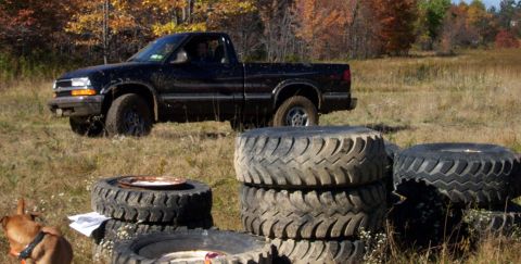 1979 Ford Bronco - A black pickup truck sits in a field surrounded by autumn foliage and stacks of large tires.