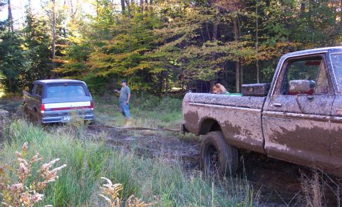 1979 Ford Bronco - A 1979 Ford Bronco is being towed out of a muddy wooded area by a Ford F-Series truck.