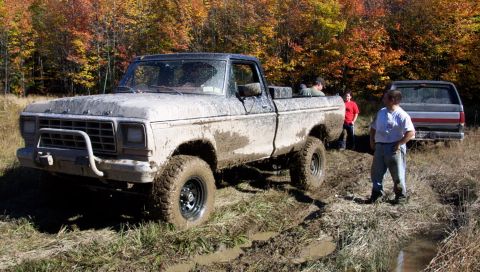 1979 Ford Bronco - A muddy 1979 Ford F-150 pickup truck is stuck in the mud with other vehicles and people nearby.