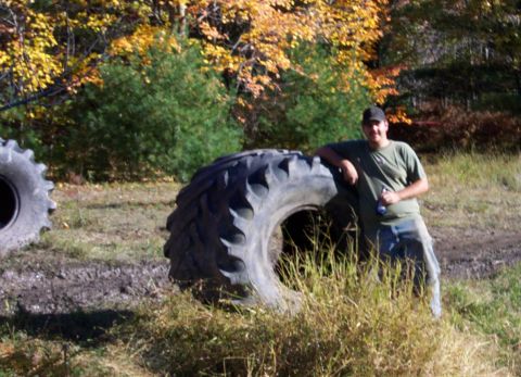 1979 Ford Bronco - Man poses with a massive tractor tire in a field during the fall season.