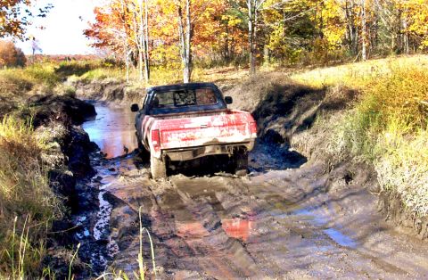 1979 Ford Bronco - This red pickup truck is stuck in a muddy ditch, surrounded by autumn trees.