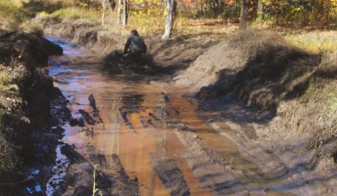 1979 Ford Bronco - A person works on a muddy, rutted trail surrounded by trees in autumn.
