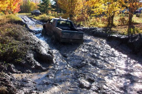 1979 Ford Bronco - A Dodge pickup truck navigates a challenging muddy terrain with another vehicle visible in the background.
